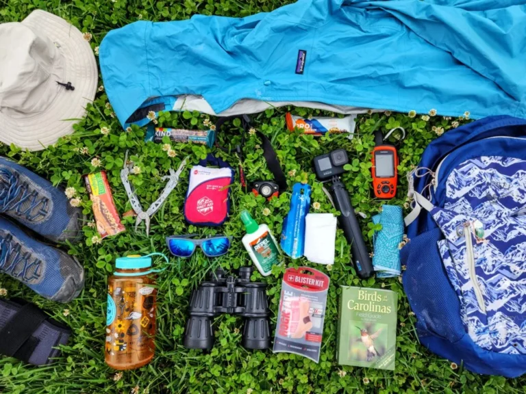 an arrangement of hiking essentials in green grass. hiking shoes, hiking backpack, rain jacket, hiking hat